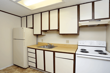 Fully equipped kitchen with a f white fridge, white stove and oven, and white and wood cabinets.